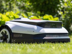 Ecovacs Goat A1600 RTK robotic lawn mower on grass with greenery in the background.