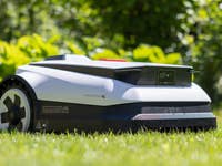 Ecovacs Goat A1600 RTK robotic lawn mower on grass with greenery in the background.