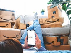 Amazon Prime logo on a mobile screen in front of piles of Amazon delivery boxes