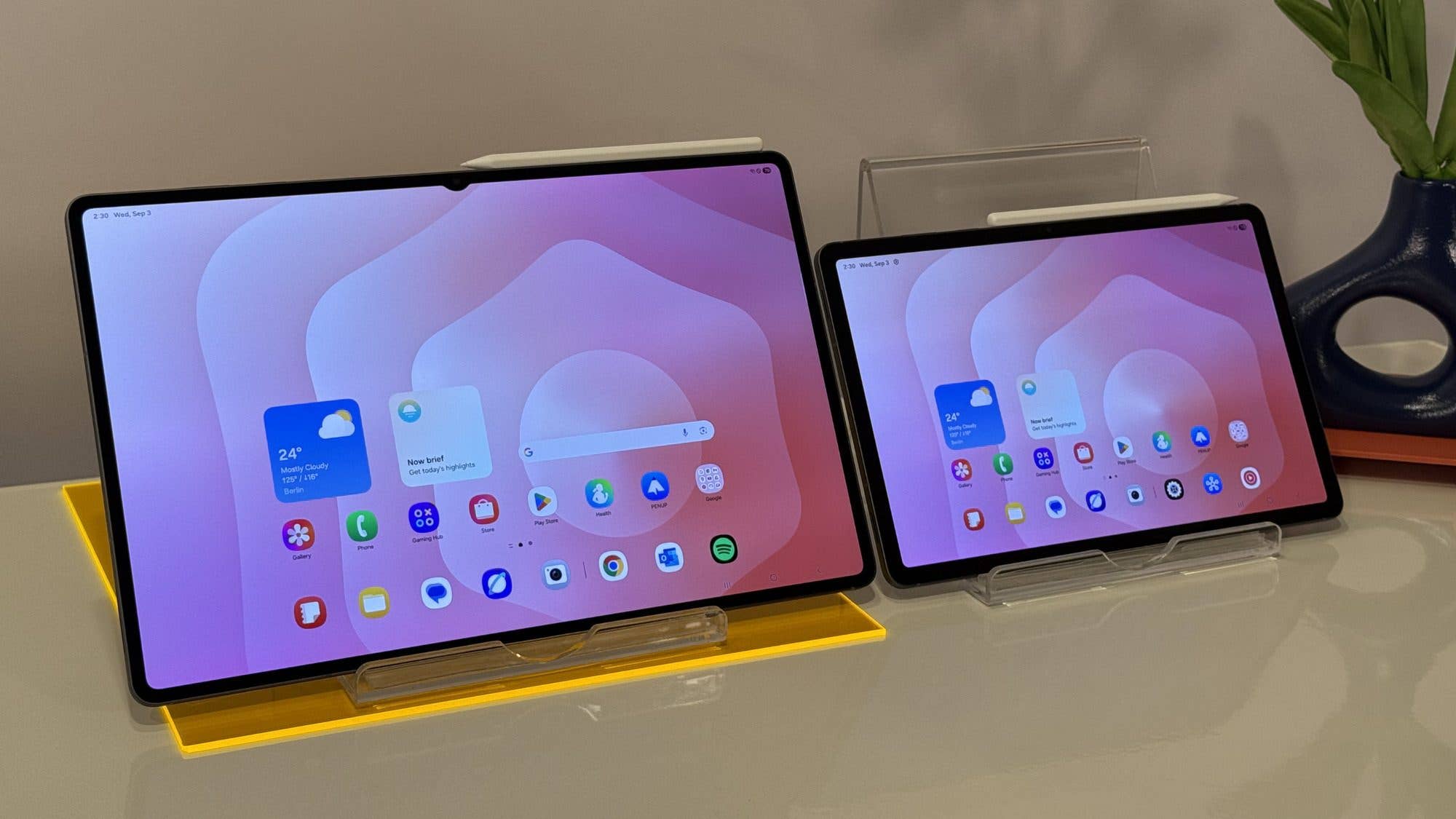 Two Samsung Galaxy Tab S11 tablets on stands, displaying a colorful home screen with various apps.