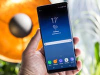 A person holding a Samsung Galaxy Note 8 smartphone displaying weather information.