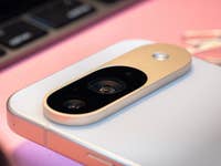 Close-up of a Google Pixel 9 smartphone's camera module on a pink surface with keys in the background.