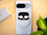 A pair of Google Pixel Buds Pro 2 in their case on a smartphone with a box beside it.