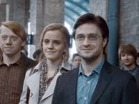 Three friends standing together in a crowded train station, smiling at the camera.