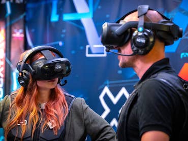 Two people wearing VR headsets engage in a virtual reality experience against a digital backdrop.