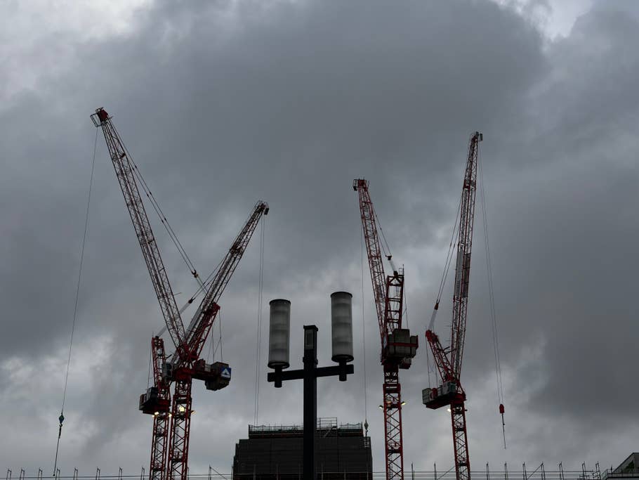 Silhouette of three construction cranes against a cloudy sky.