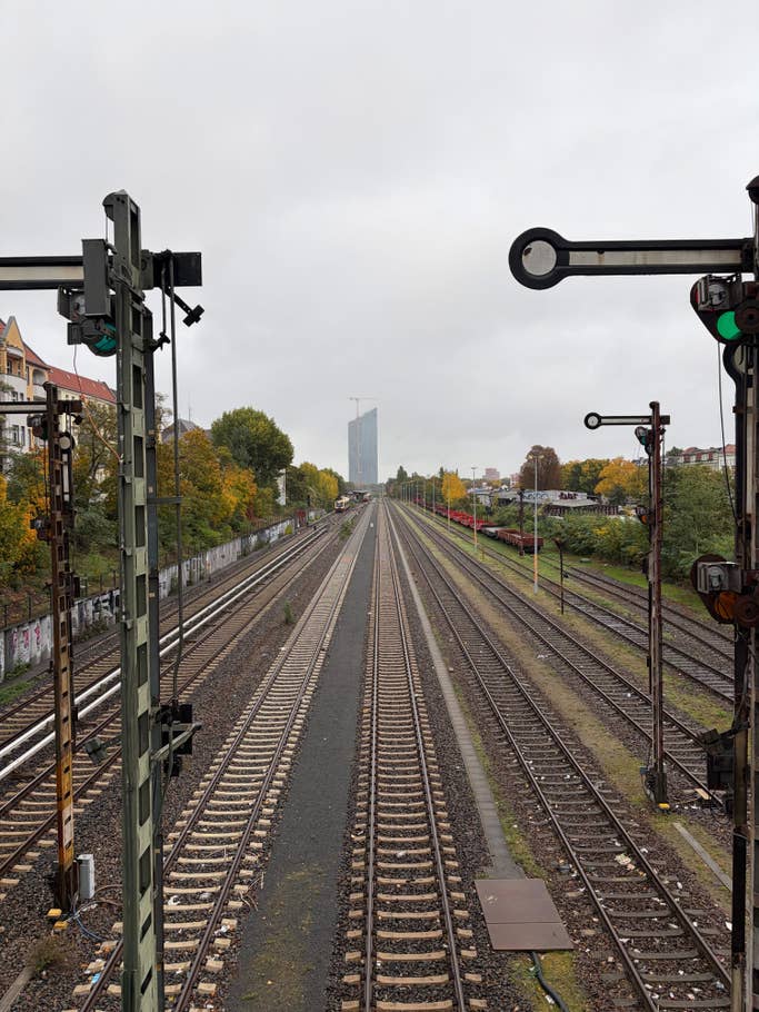 A railway stretching into the distance under a cloudy sky, with green signals and city building.