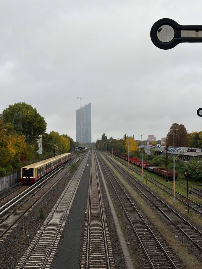Railroad tracks leading to a train station with a building in the background under a cloudy sky.