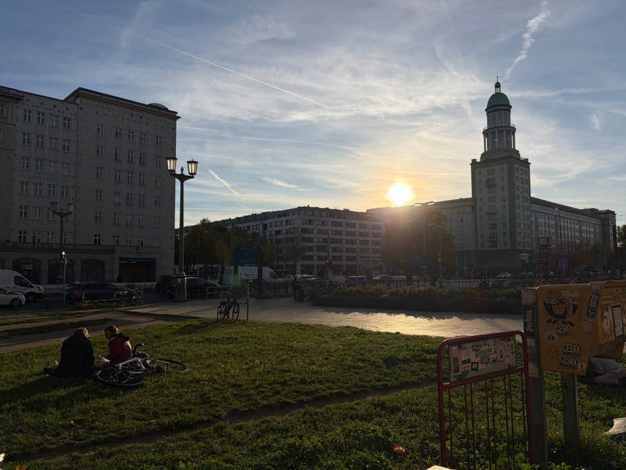 Sunset over a cityscape with people on the grass with bicycles nearby.