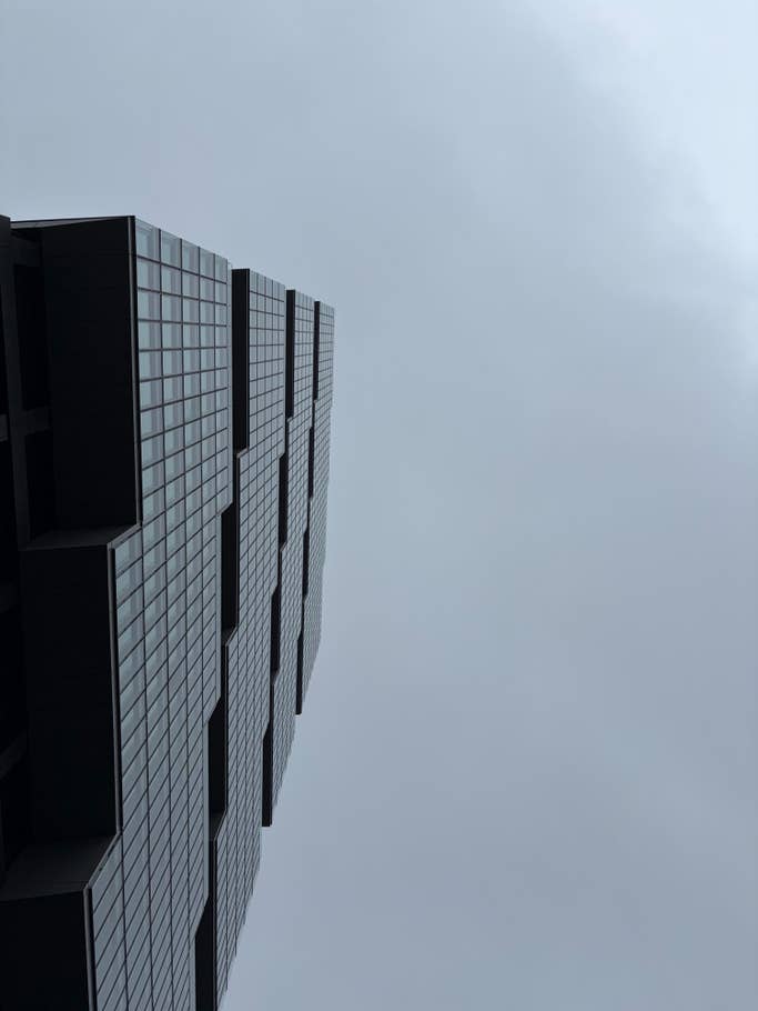 A tall building complex with a glass facade against a cloudy sky.