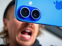 Close-up of a blue Apple iPhone 16 camera with a person shouting in the background.