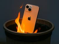 An iPhone partially submerged in flames inside a trash bin.