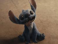 A small blue alien creature with large ears and big eyes, sitting and sticking out its tongue.