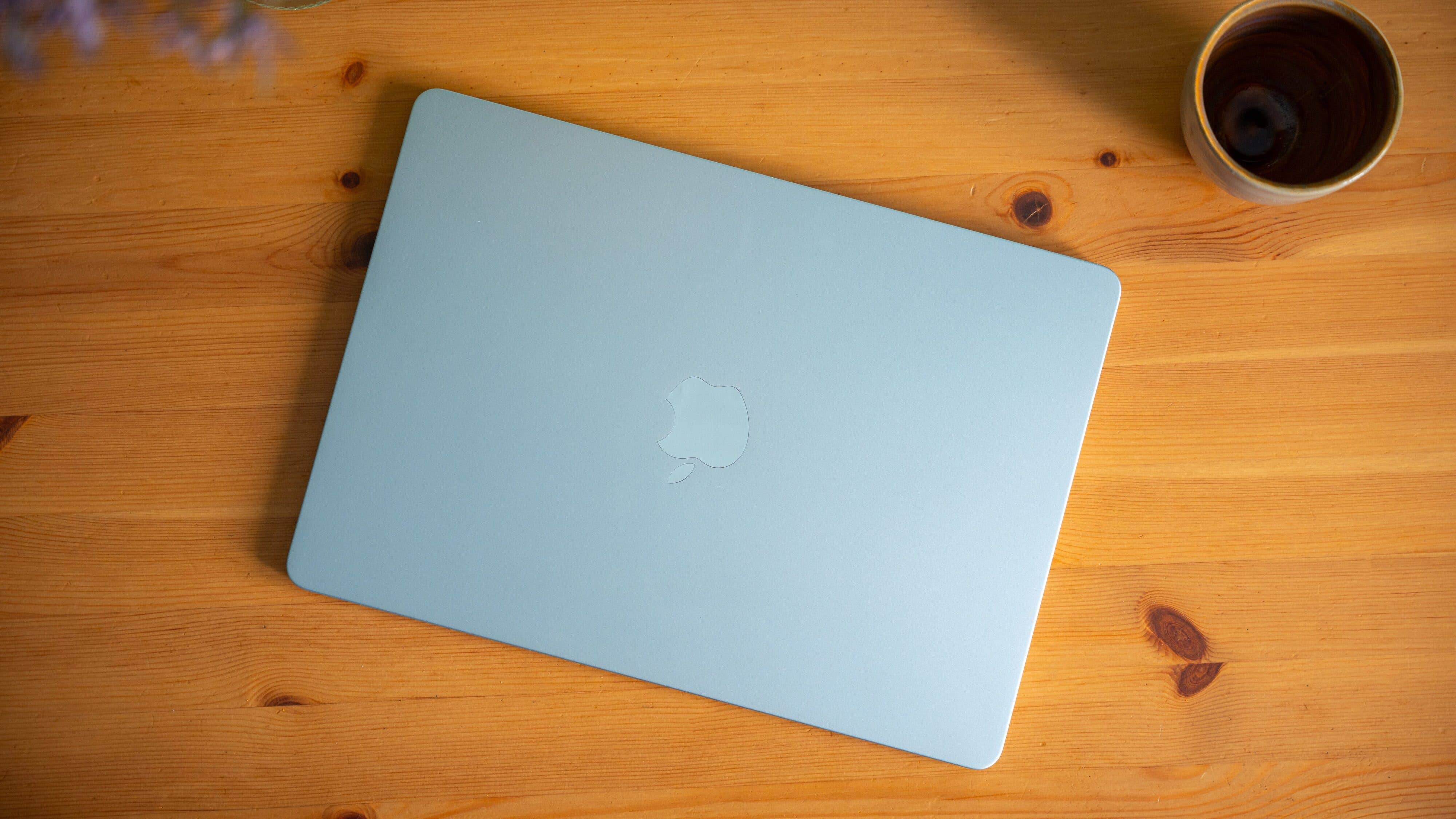 A Sky Blue Apple MacBook Air lies on a wooden table next to a cup.