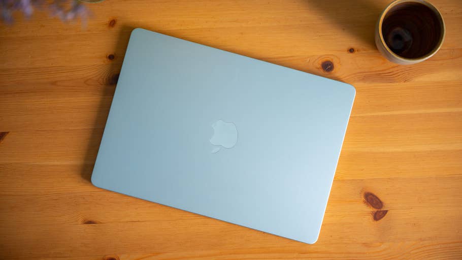 A Sky Blue Apple MacBook Air lies on a wooden table next to a cup.