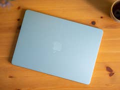 A light blue Apple MacBook Air resting on a wooden table next to a cup.