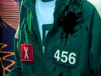 A person wearing a green tracksuit with the number 456 and a red 'X' badge, stained with splashes.