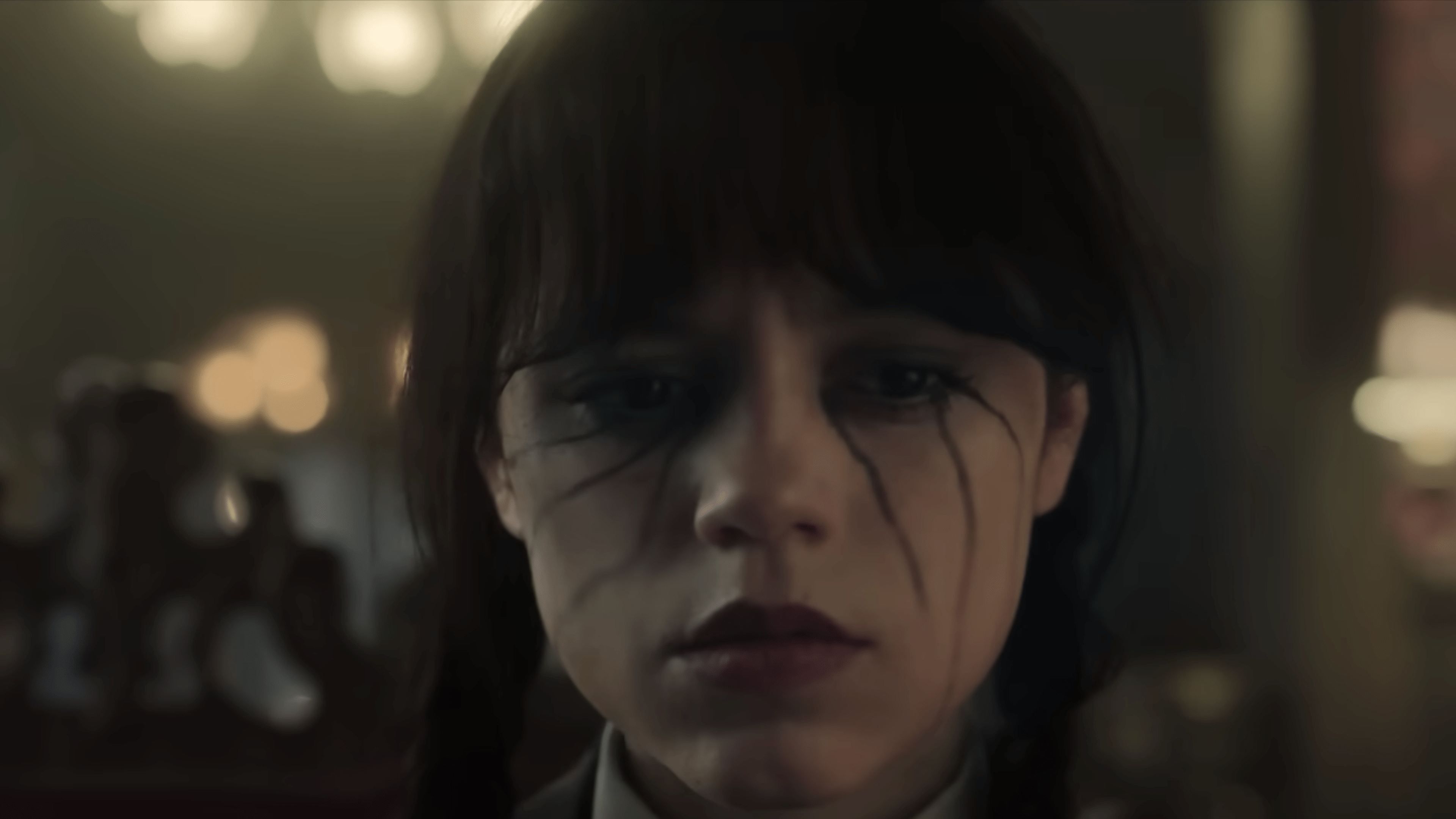 A close-up of a girl with dark makeup and braids, looking somber.