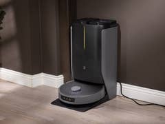 A robotic vacuum docked at its charging station against a dark wall.