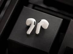 White Apple AirPods on a black background with stacked boxes.