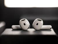 Two white Apple AirPods positioned on a dark surface with a soft background light.