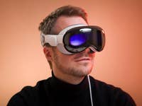 A person wearing Apple Vision Pro augmented reality headset against a warm background.