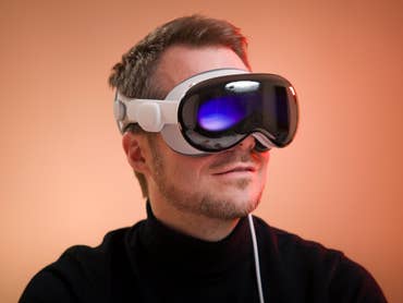 A person wearing Apple Vision Pro augmented reality headset against a warm background.