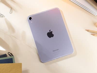 Apple iPad Mini 7 showing the back with logo on a desk surrounded by papers and pencils.