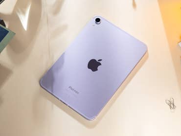 Apple iPad Mini 7 in lilac color, displayed on a desk with stationery items.