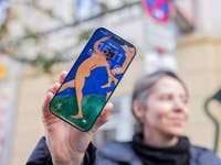 A person holding an iPhone 17 displaying artwork as the lock screen with the time 15:11.