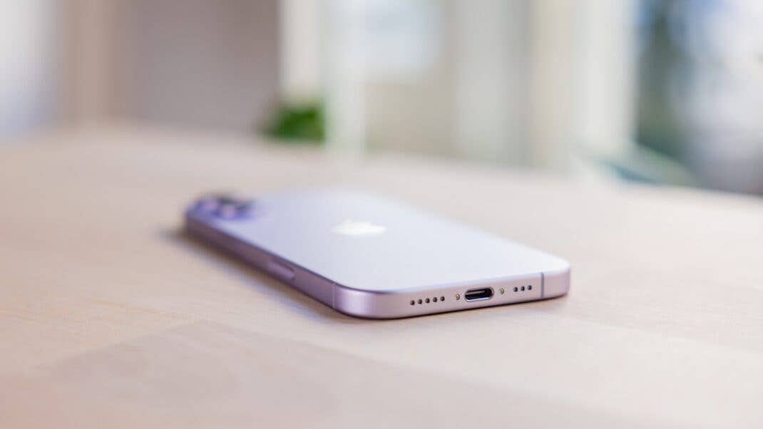 A close-up of the Apple iPhone 17, showing its purple back and charging port on a wooden surface.