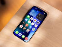 An iPhone with a colorful app layout on a wooden surface that displays weather and calendar widgets.