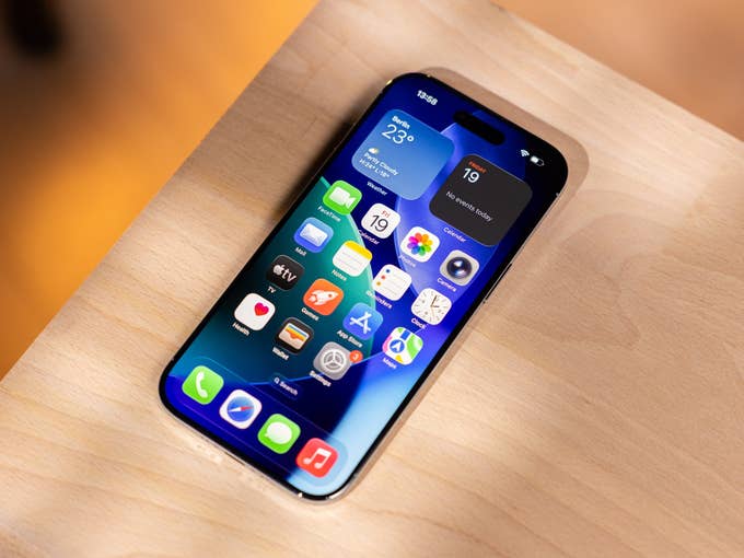 An iPhone with a colorful app layout on a wooden surface that displays weather and calendar widgets.