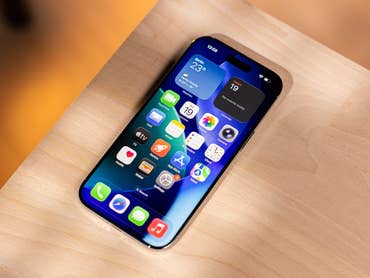 An iPhone with a colorful app layout on a wooden surface that displays weather and calendar widgets.