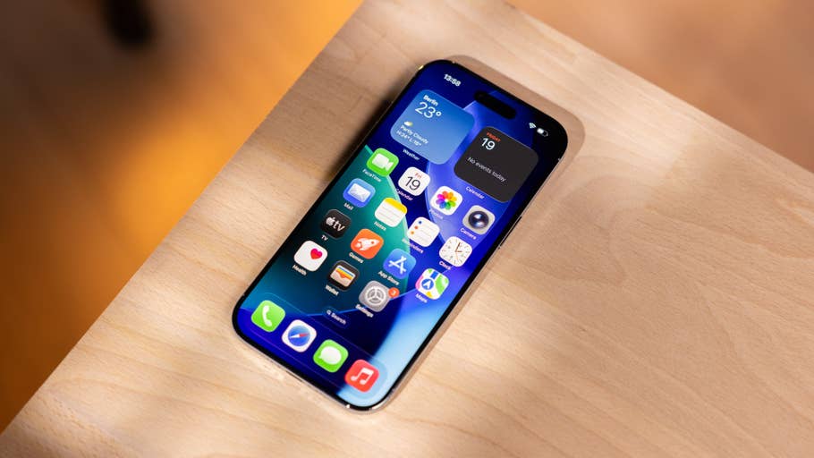 An iPhone with a colorful app layout on a wooden surface, displaying weather and calendar widgets.