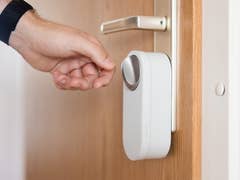 A hand reaching for a smart door lock installed on a wooden door.