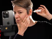A person using a Bebird tool to clean their ear while a smartphone is set up to record the process.