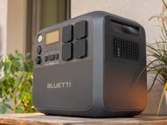 A Bluetti AC200L portable power station on a wooden table with a plant and a lantern nearby.