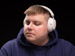 A person wearing Bose QC Ultra headphones, eyes closed, appears focused and relaxed against a black background.