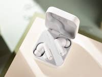 White wireless earbuds in their charging case on a light surface.