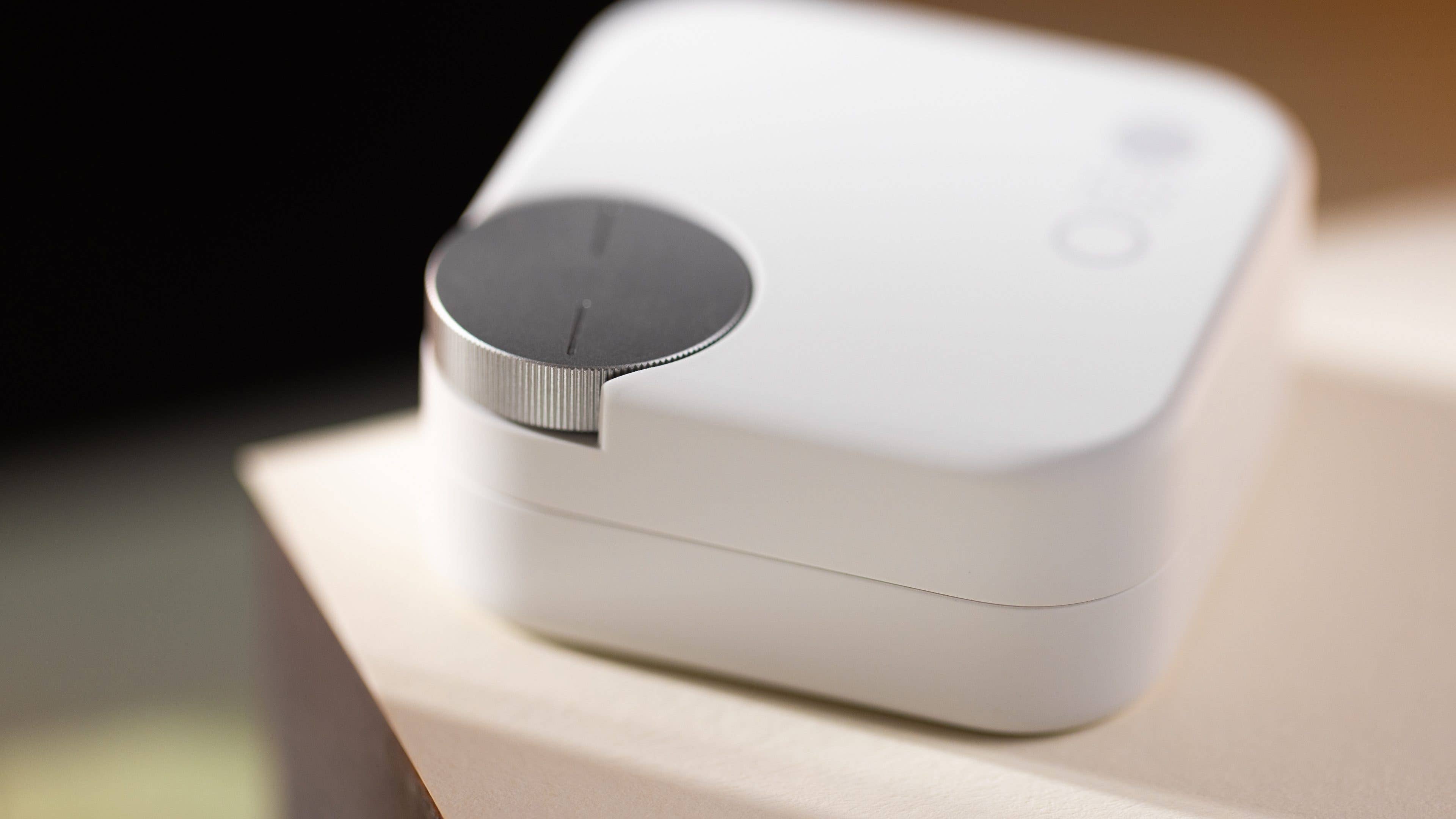 A compact white device with a circular control dial on top, resting on a light-colored surface.