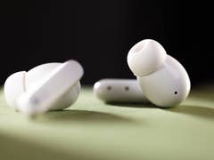 Wireless earbuds on a green surface, showcasing a sleek white design.