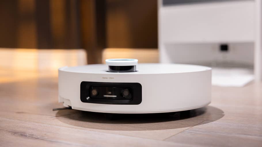 A white robot vacuum cleaner with sensors on a wooden floor.
