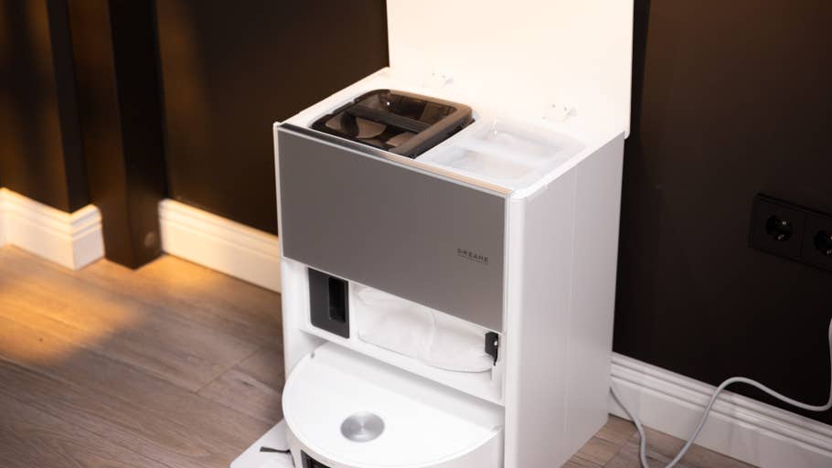 A white unit with a gray front, storage compartments, and a rounded base against a dark wall.