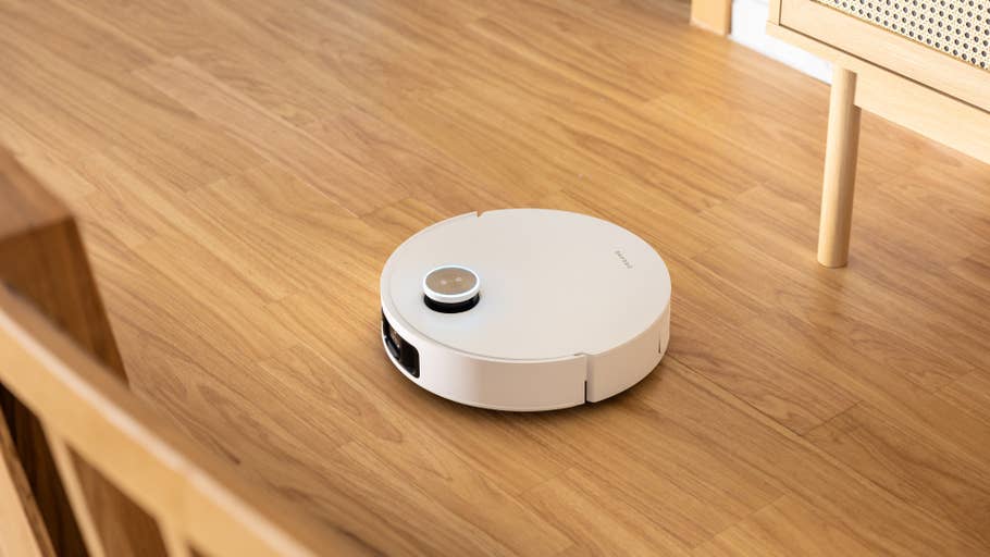A Dreame X50 Ultra robot vacuum cleaner on a wooden floor near some furniture.