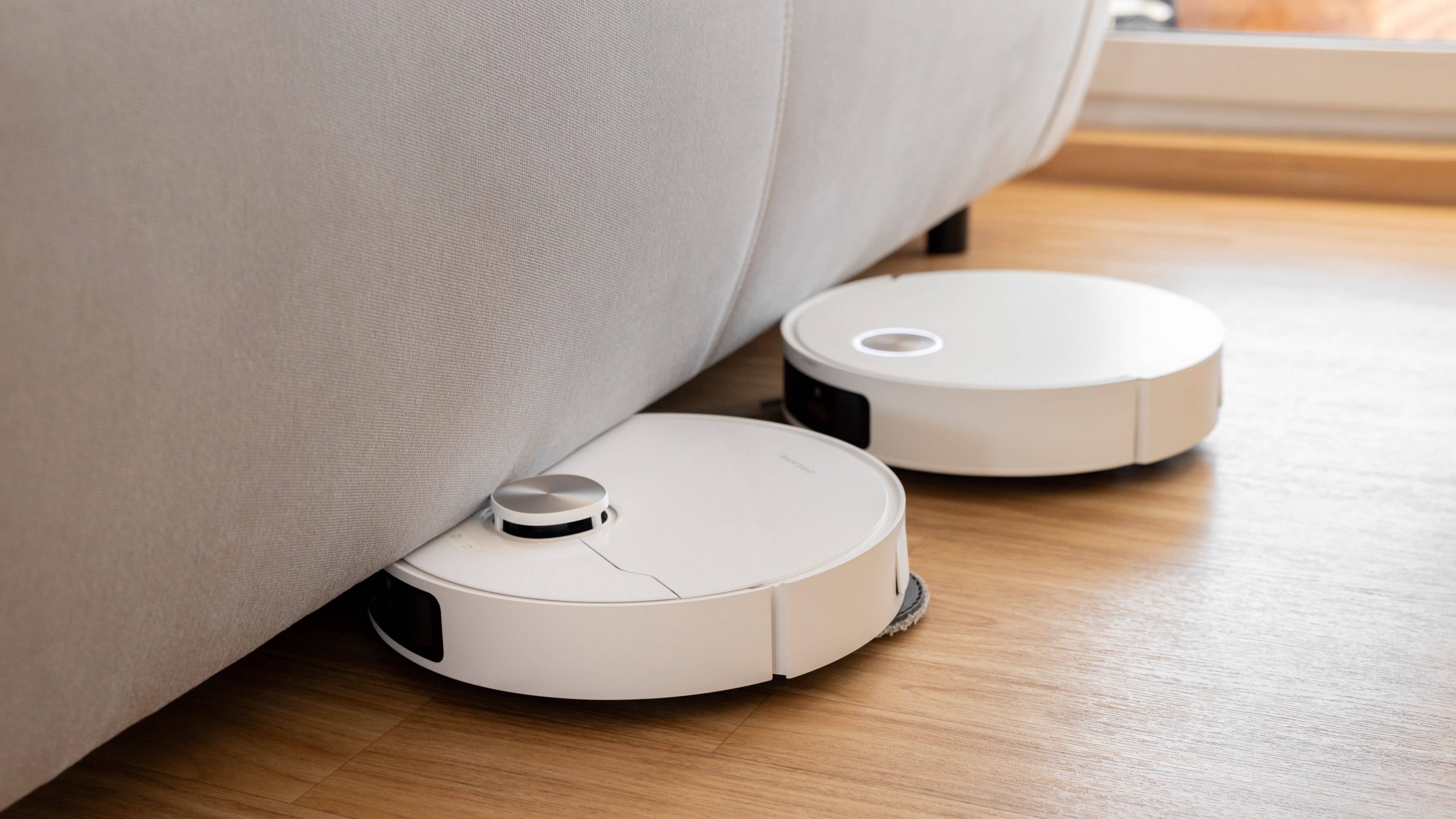 Two Dreame X50 Ultra robotic vacuums positioned under a couch on a wooden floor.