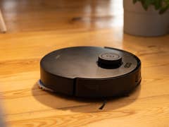 A black Ecovacs Deebot T30s Combo robot vacuum on wooden floor.
