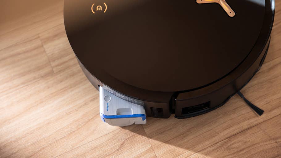 Robot vacuum cleaner with stylish black design and attached side container, on a wooden floor.