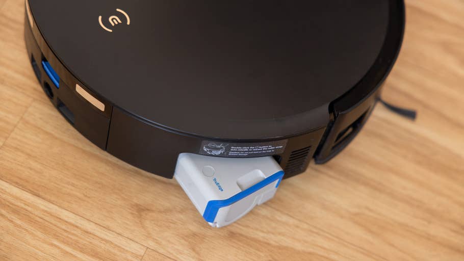 A black Ecovacs Deebot X8 Pro Omni with its removable dust container on a wooden floor.