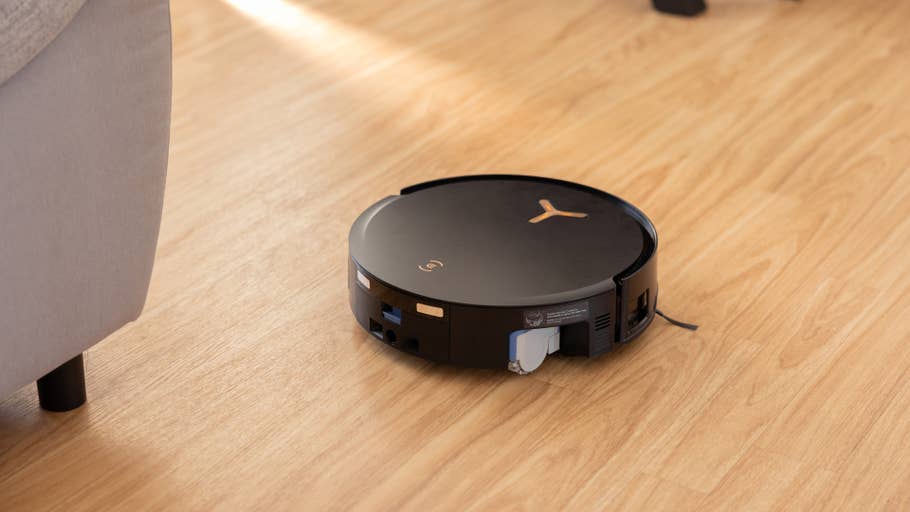 A black Ecovacs Deebot X8 Pro Omni robot vacuum cleaner on a wooden floor next to a sofa.